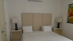 A bedroom with a bed, two nightstands, two lamps, and a painting on the wall. - Departamento cerca del mar 103 (Puerto Aventuras)