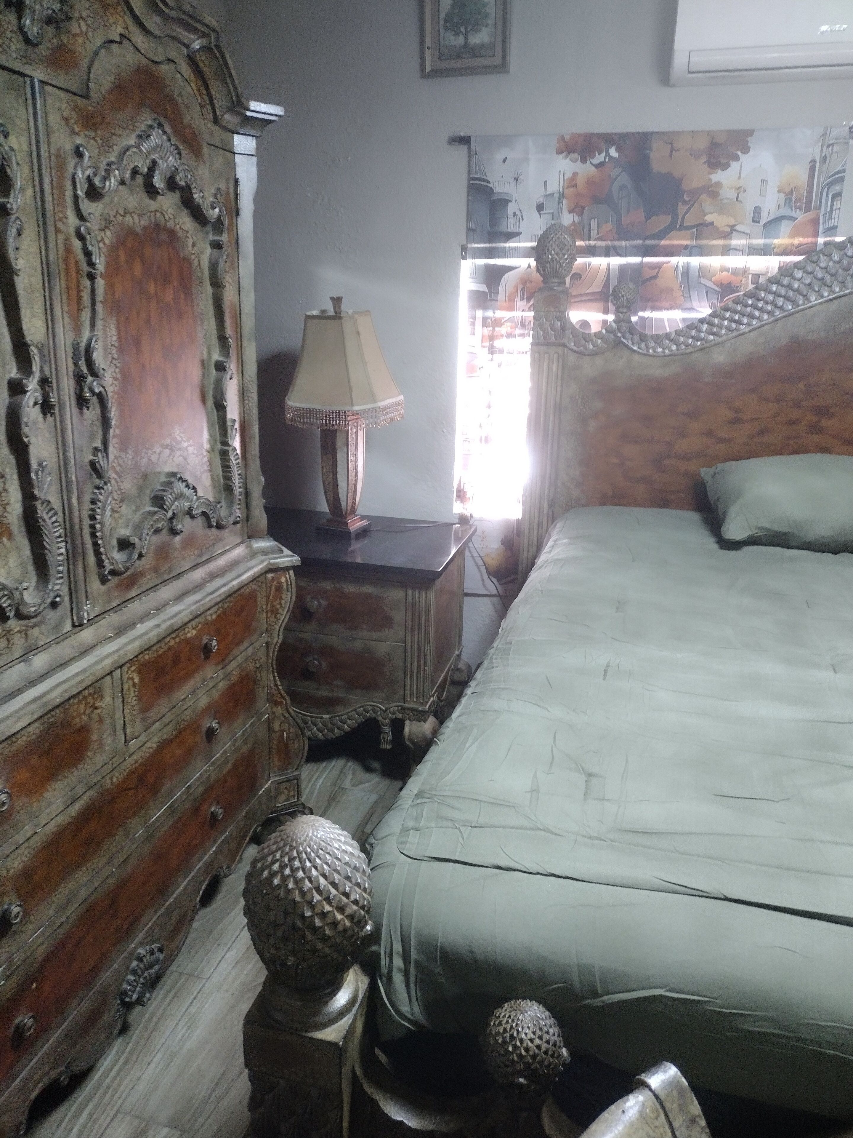 A bedroom with a bed, a dresser, a lamp, and a decorative mirror.