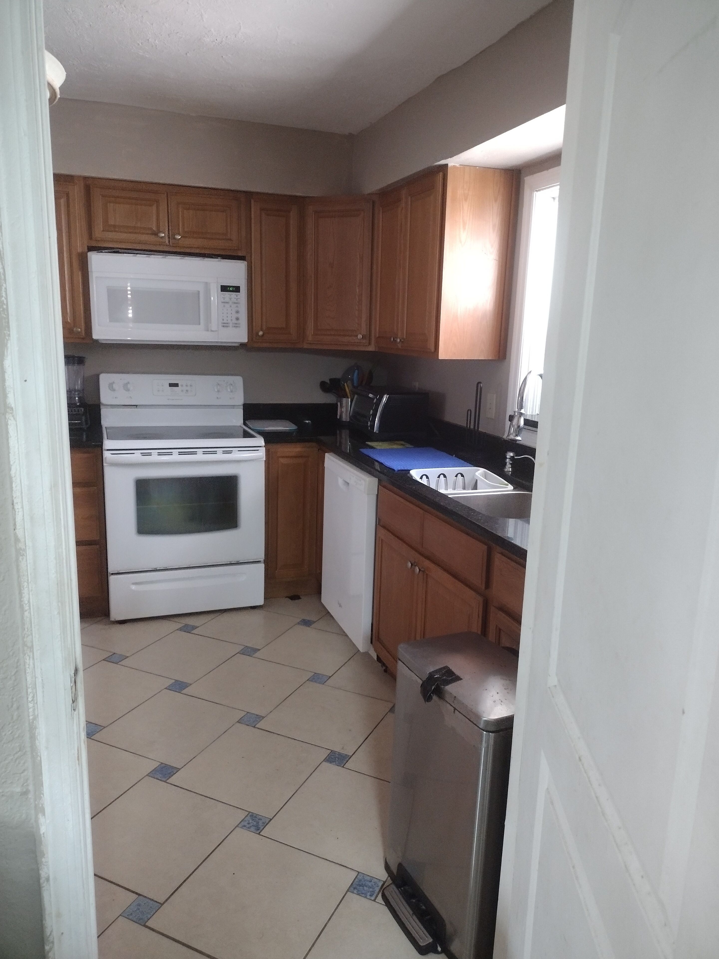 A compact kitchen with wooden cabinets, a microwave, a stove, a dishwasher, and a refrigerator.