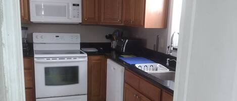 A compact kitchen with wooden cabinets, a microwave, a stove, a dishwasher, and a refrigerator.