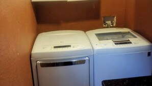 A laundry area with two white washing machines and a dryer, a wooden floor, and white cabinets above. - Pleasant 1-bedroom house with AC in sunny Orlando (Orlando)