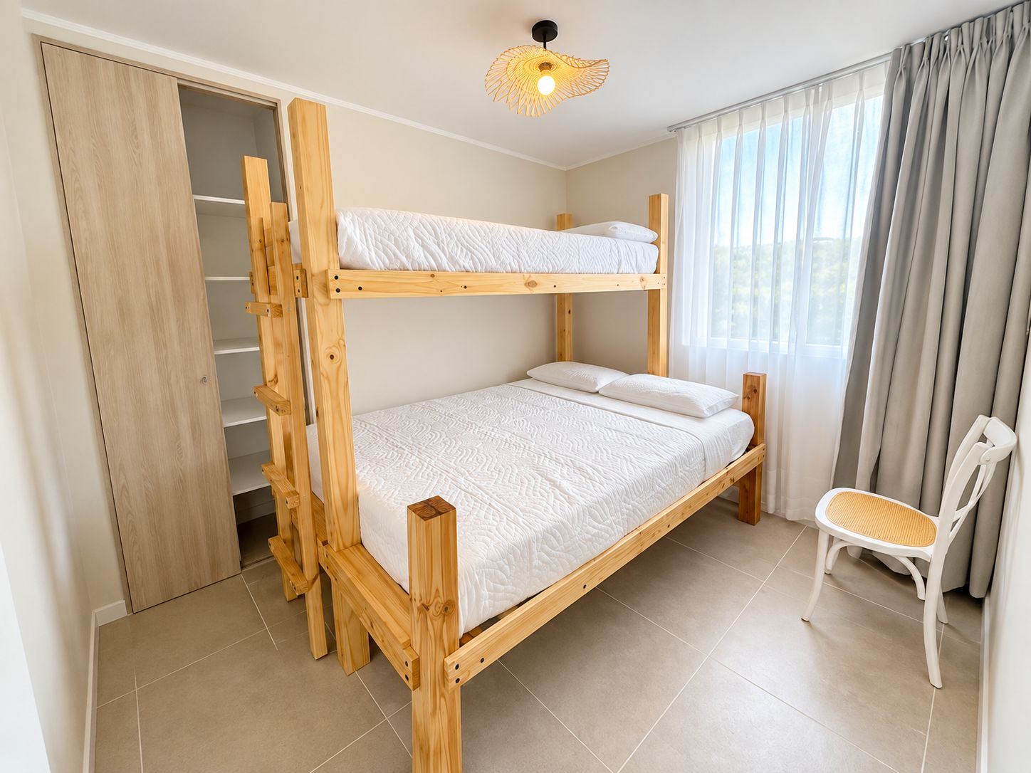 Un lit superposé avec une échelle, une chaise et une fenêtre avec des rideaux.