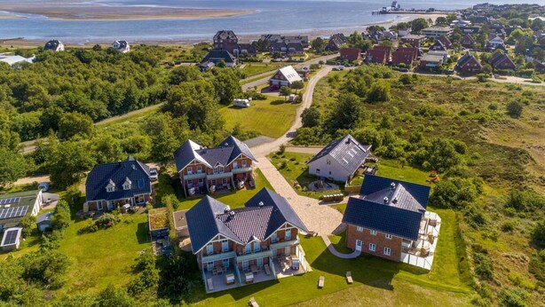 An aerial view of a residential area with houses, a beach, and a pier in the background. - Kniepsand vacation apartment, quiet but very centrally located on the dunes (Wittdün auf Amrum)