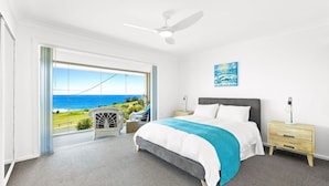 A bedroom with a bed, a nightstand, a lamp, and a view of the ocean. - Golfers View Penthouse (Narooma)