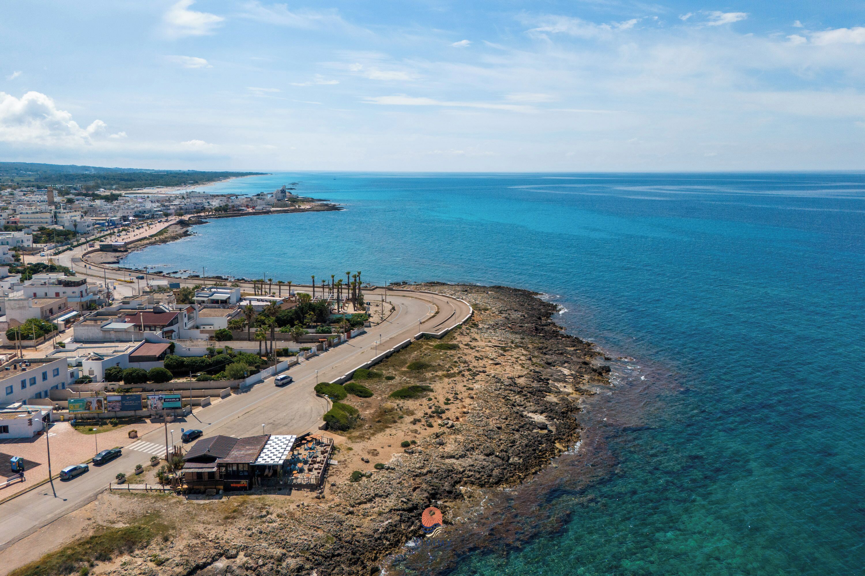 An aerial view of a coastal town with a beach, buildings, and a road.
