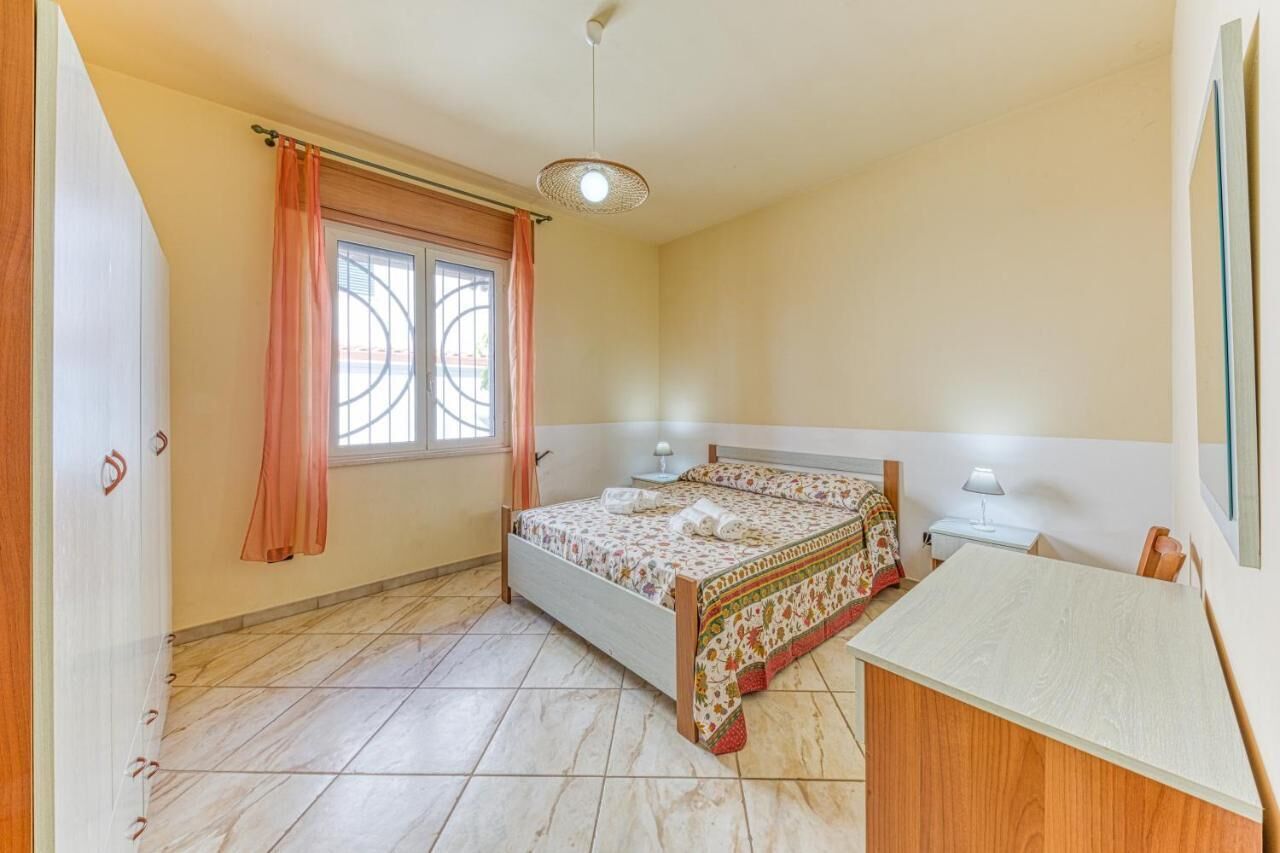 Ein Schlafzimmer mit einem Bett, Nachttischen, einem Schreibtisch, einem Fenster mit Vorhängen und einer Pendelleuchte.