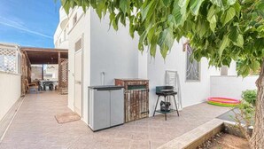 Zona exterior amb una barbacoa, una taula i cadires.