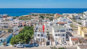 Zona residencial costanera amb una combinació d'arquitectura moderna i tradicional, incloent un edifici blanc prominent amb teulada vermella al primer pla.