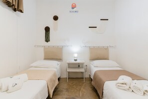 Une chambre d’hôtel avec deux lits, une petite table de chevet avec une lampe et une étagère fixée au mur.