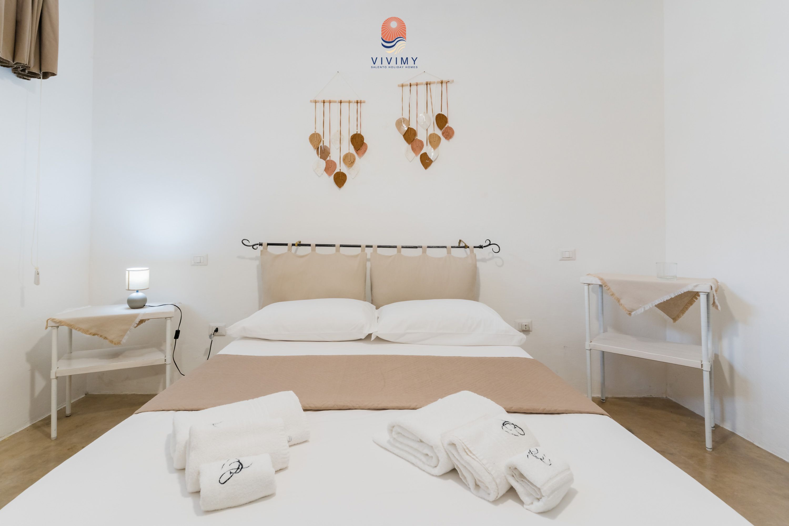 Una camera d'albergo con un letto, due comodini, un elemento decorativo a parete e una lampada da comodino.