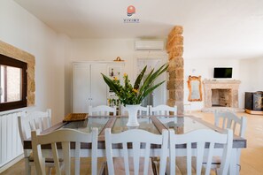 Een eetgedeelte met een glazen tafel en witte stoelen, een stenen zuil en een open haard.