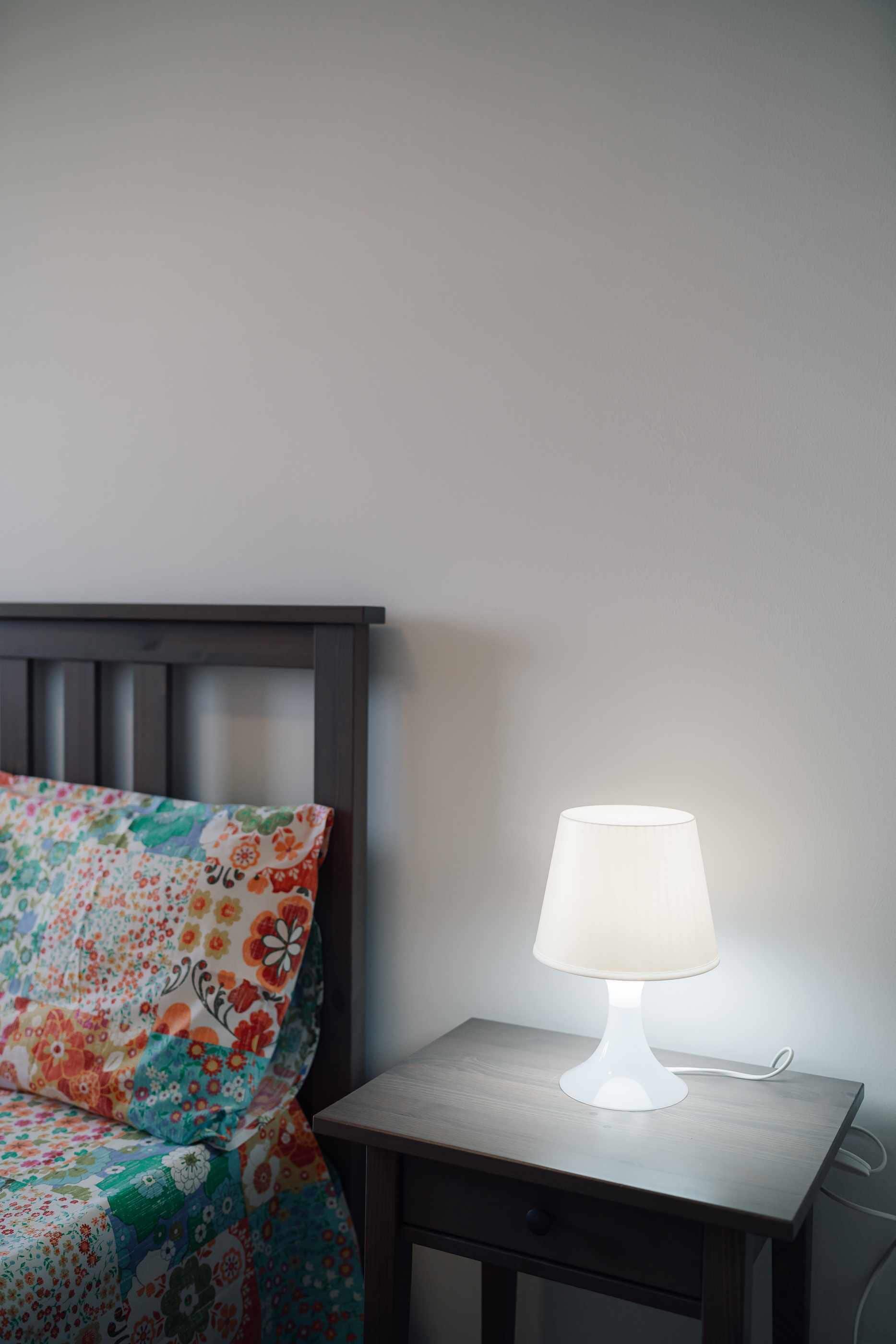 Ein Bett mit einer decke mit Blumenmuster, ein Nachttisch mit einer weißen Lampe und ein dunkles Holz-Kopfteil.