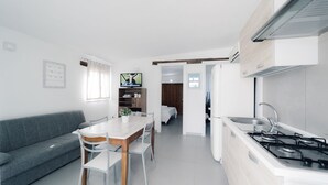A modern kitchen with a dining area, a grey sofa, and a TV in the background. - Villa Sole By Vivimy (Parabita)