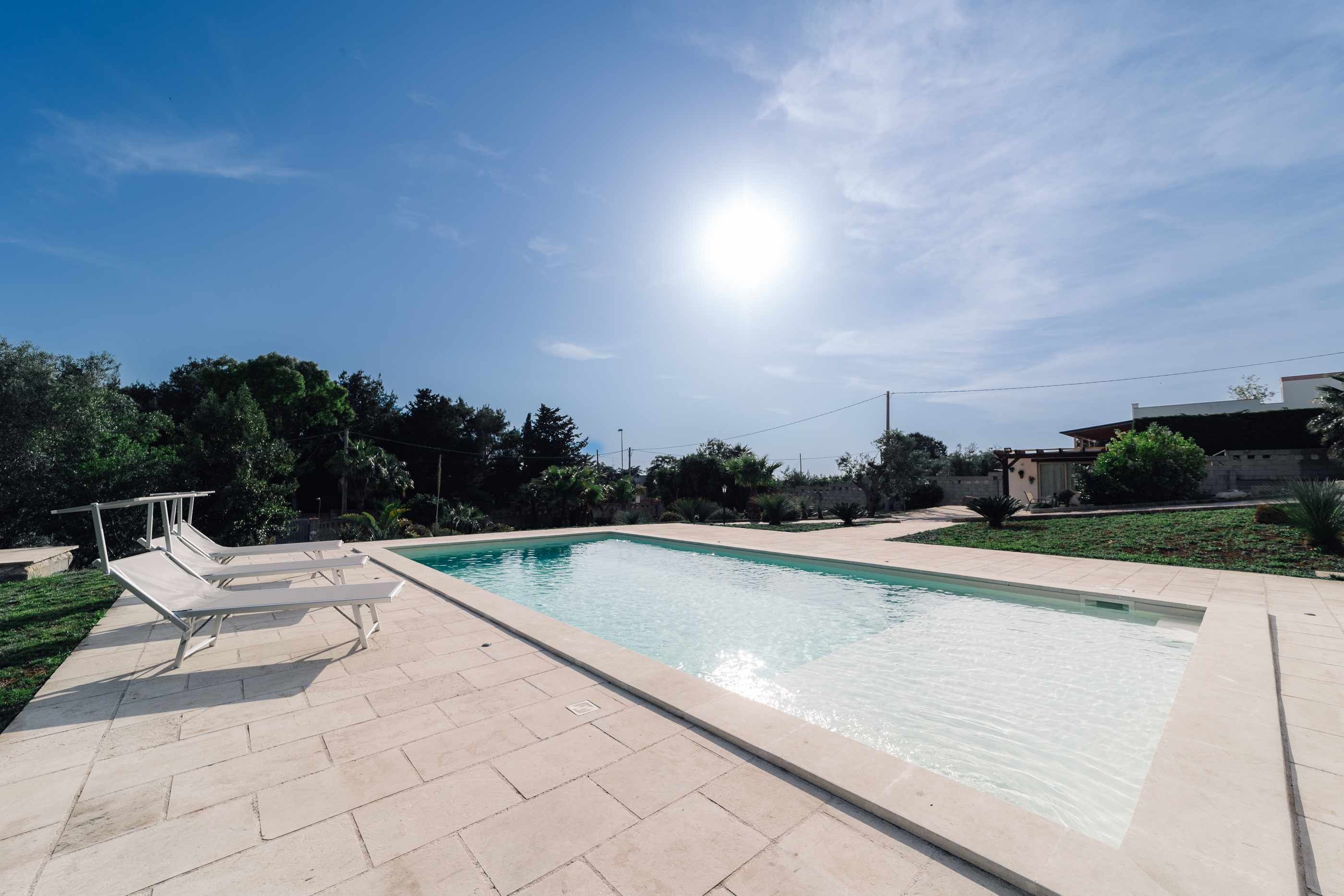 A rectangular swimming pool with a tiled deck and lounge chairs.