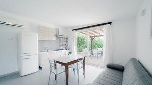 A modern kitchen with white cabinetry, a dining table with chairs, and a gray sofa. - Villa Sole By Vivimy (Parabita)