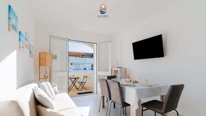 En moderne stue med sofa, spisebord, stole og et fjernsyn monteret på væggen.
