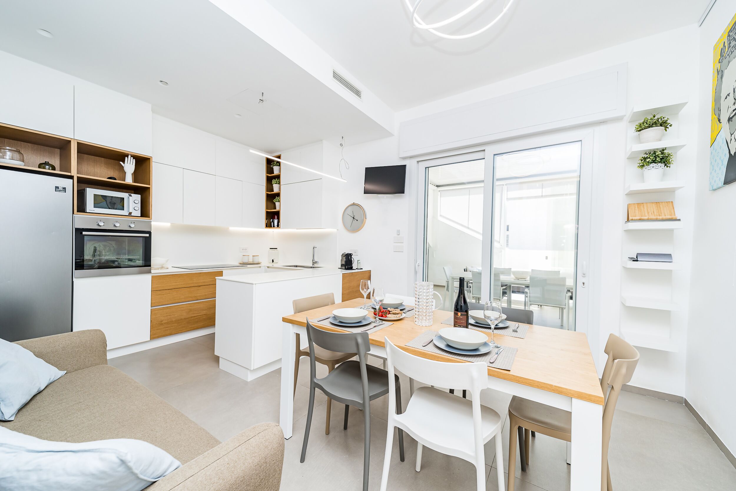 A modern kitchen with white cabinets, a microwave, and an oven. There is a dining area with a wooden table and chairs.