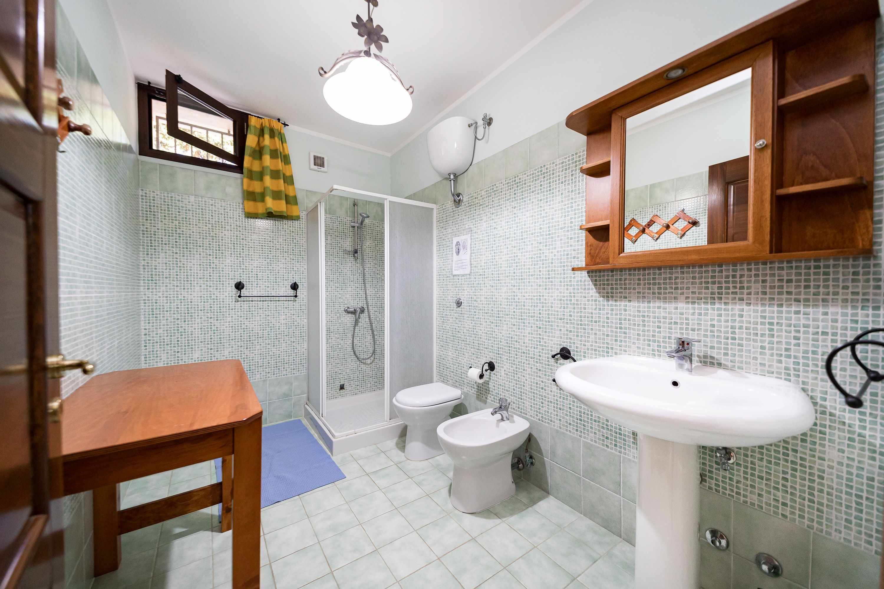 A bathroom with a shower, toilet, bidet, and sink, featuring tiled walls and a wooden vanity.