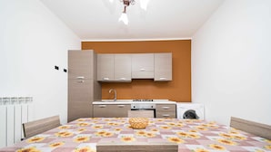 Une chambre à coucher de taille réduite, comprenant un lit, une tête de lit en bois, une petite table et un coin cuisine avec des placards et un évier.