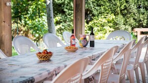 Un espace extérieur abrité, aménagé pour les repas, avec une table dressée pour six personnes, entourée de chaises en plastique blanches.