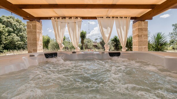 A hot tub under a wooden pergola with white curtains, surrounded by greenery and a clear sky. - Trullo Puglia by Vivimy (Salve)