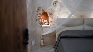 A bedroom with a bed, a small table with a lamp, and a decorative archway. - Trullo Puglia by Vivimy (Salve)