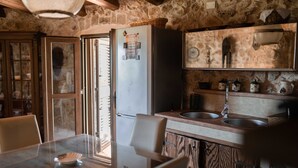 A rustic kitchen with a stone wall, wooden cabinets, a glass dining table, and a refrigerator. - Trullo Puglia by Vivimy (Salve)