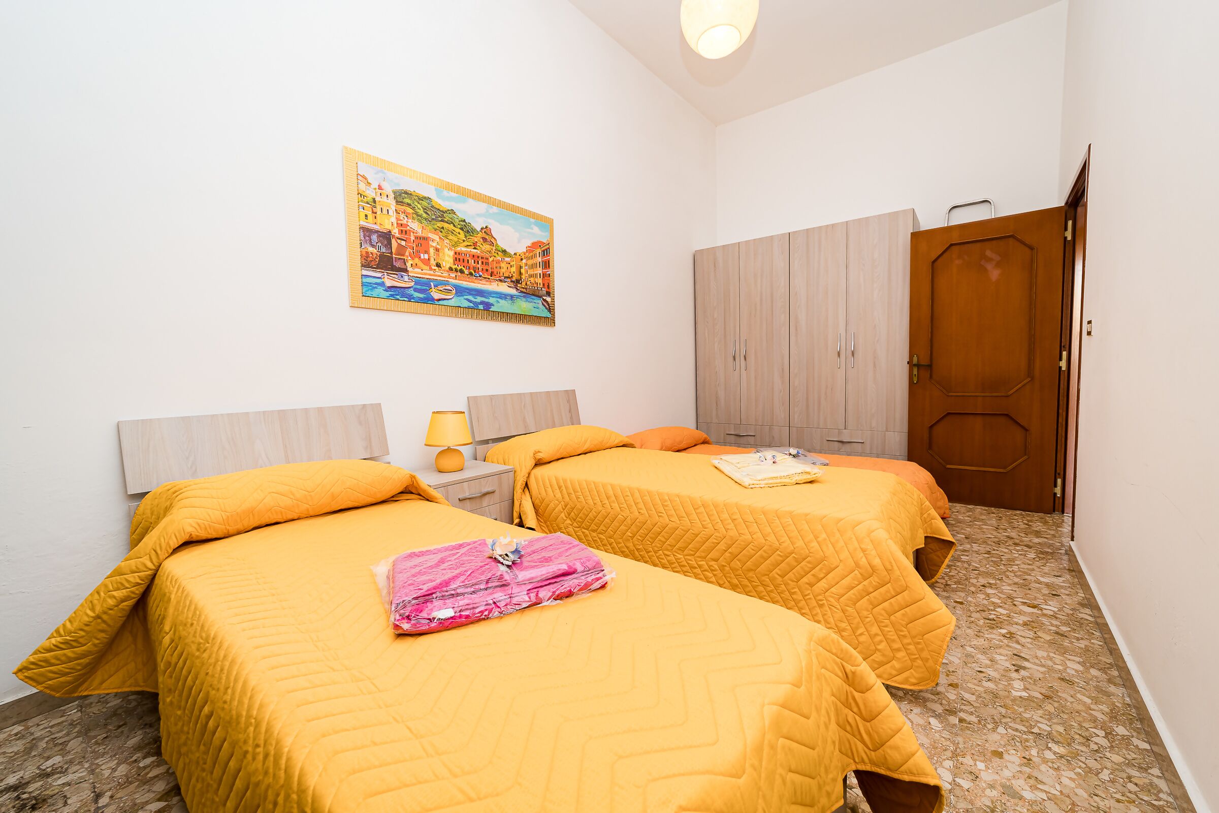 Une chambre avec deux lits, une armoire en bois, un tableau au mur et une porte.