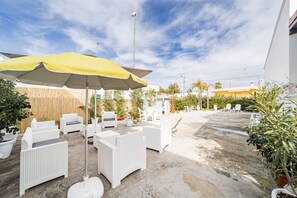 Un espace extérieur aménagé avec des meubles en osier blanc et un parasol jaune.