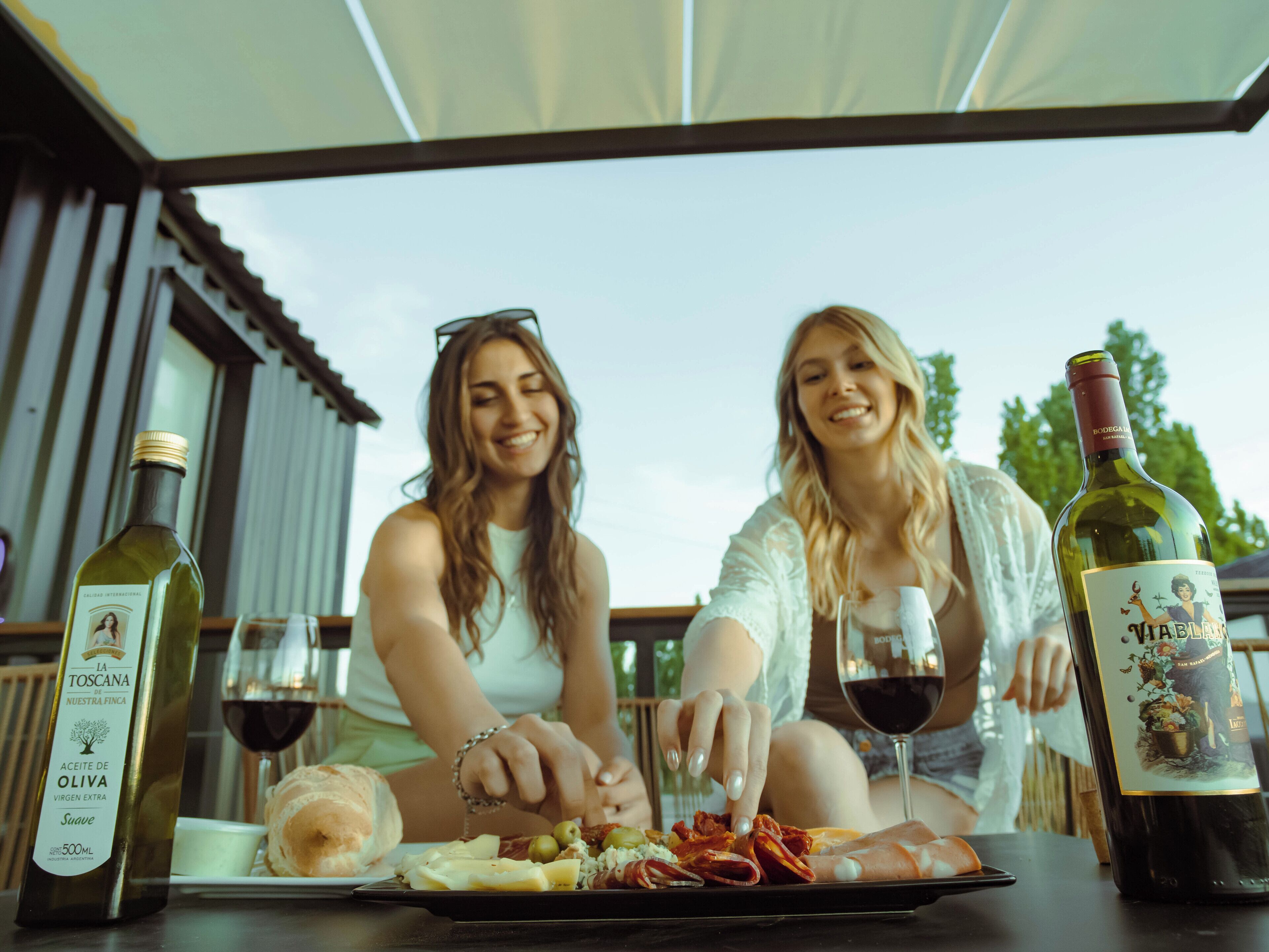 Two people dining outdoors with wine bottles and a tray of food.
