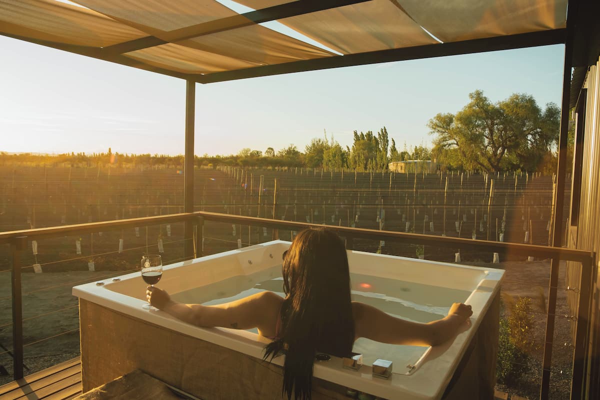 A person relaxing in a hot tub with a view of a vineyard.