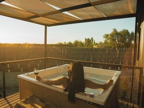A person relaxing in a hot tub with a view of a vineyard.