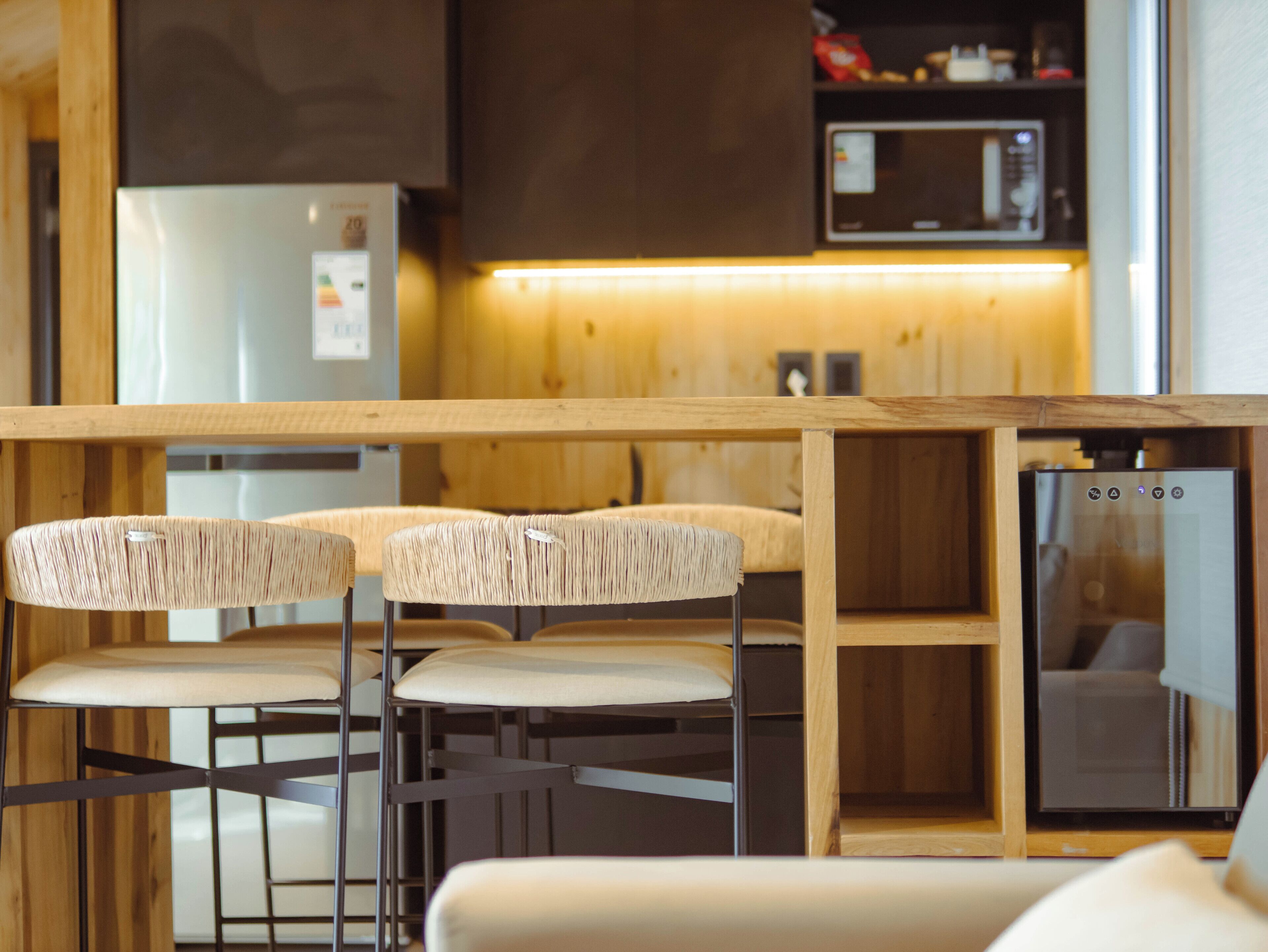 Una cocina con mostrador de madera, dos sillas con asientos de mimbre, un microondas y un refrigerador.