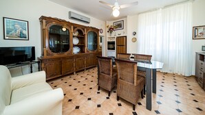 Ein Wohnzimmer mit Fernseher, einem Esstisch mit Stühlen, einer Couch, einem Deckenventilator und einer Vitrine mit Dekoration.