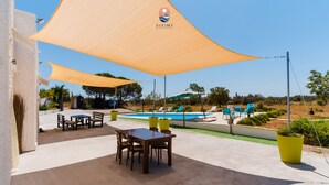 Un patio con piscina, mobiliario exterior y estructuras de sombra.