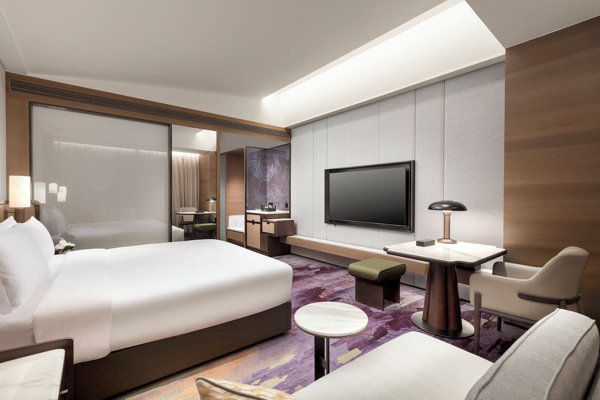 Une chambre d’hôtel moderne avec un grand lit, un bureau, une chaise, une télévision et une petite table ronde.