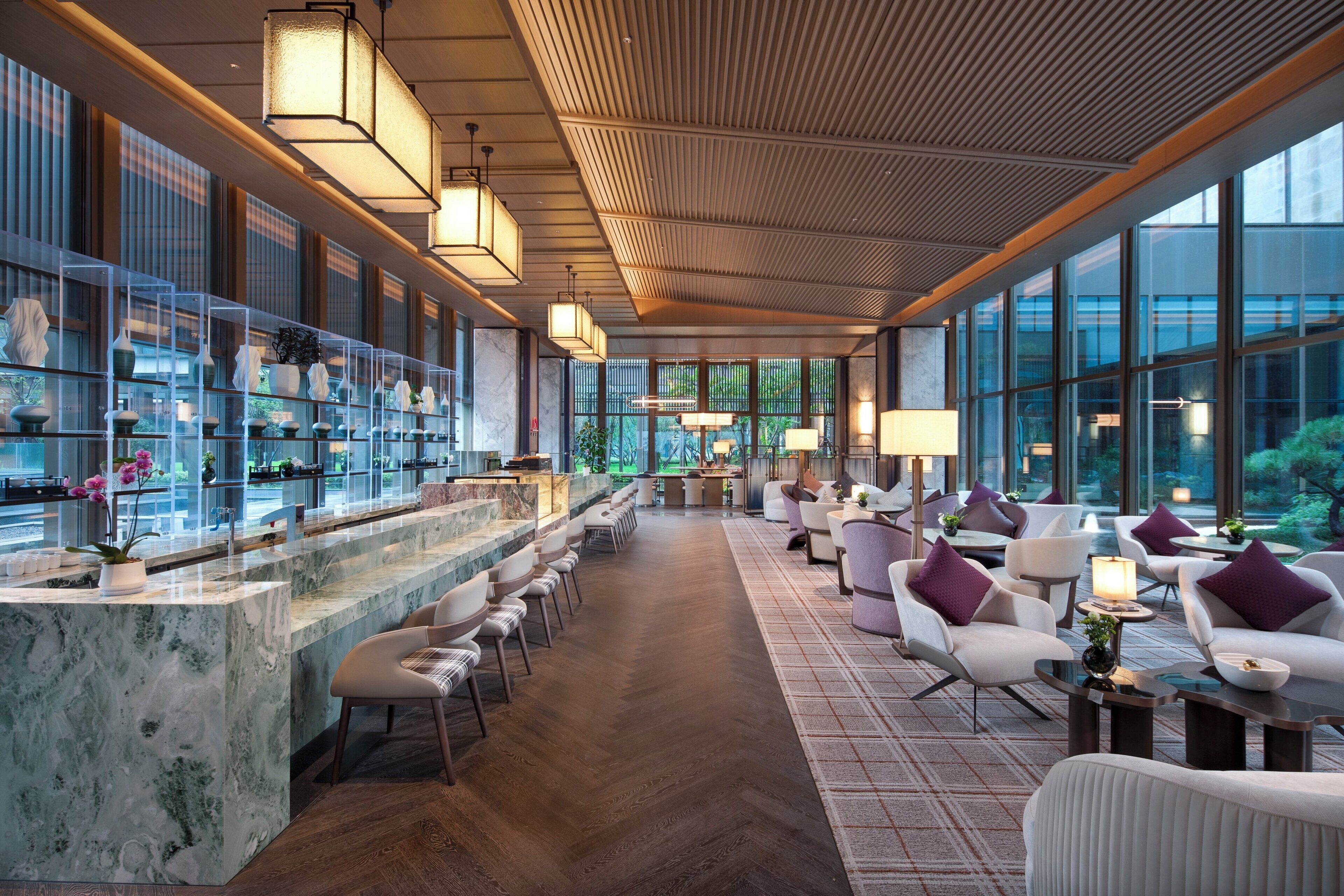 Zona de bar moderna con mostrador de mármol, asientos y ventanas amplias con vistas a la vegetación.