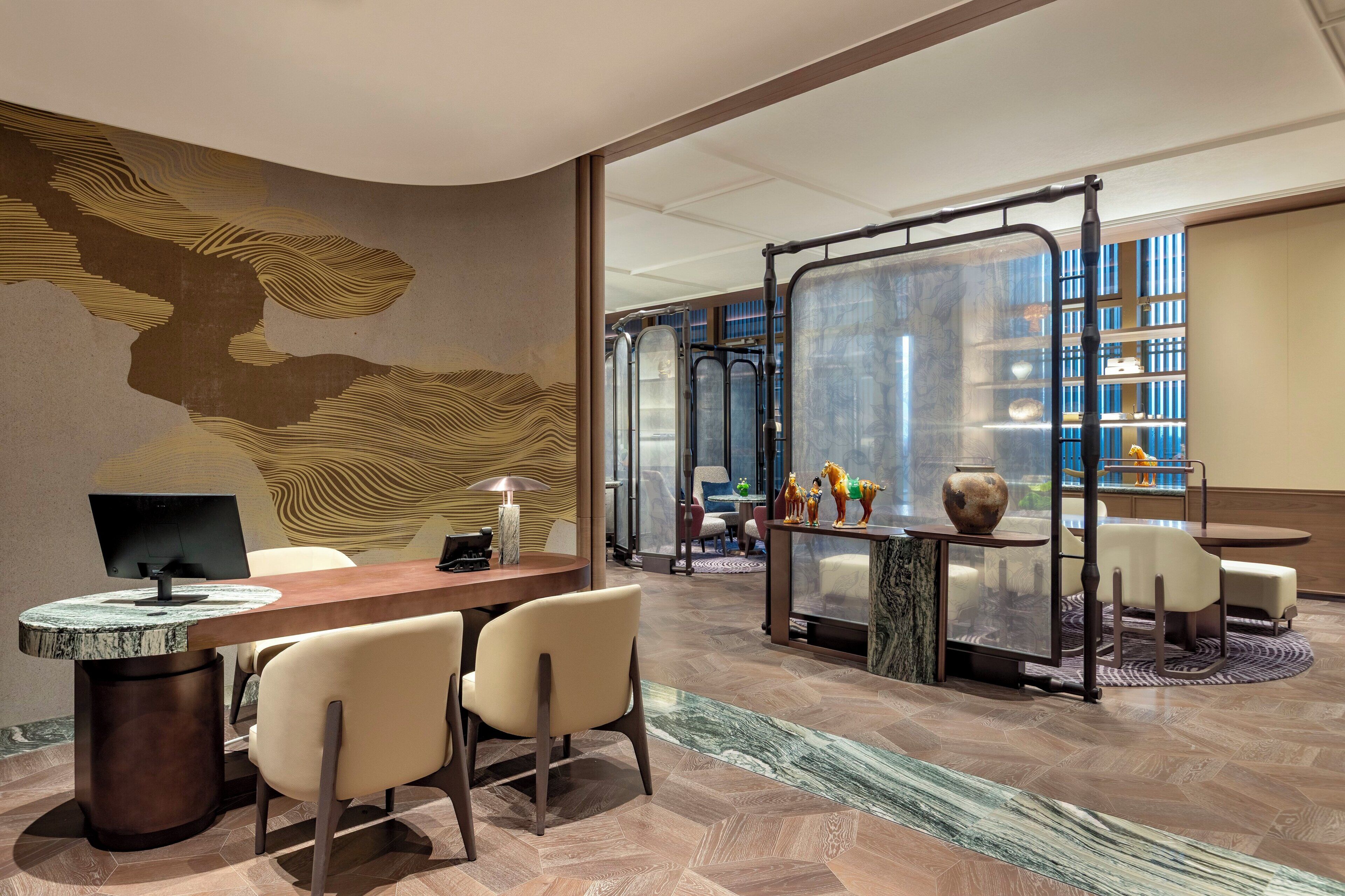 Een moderne hotellobby met een receptiebalie, een zithoek en uitzicht op de stad door grote ramen.