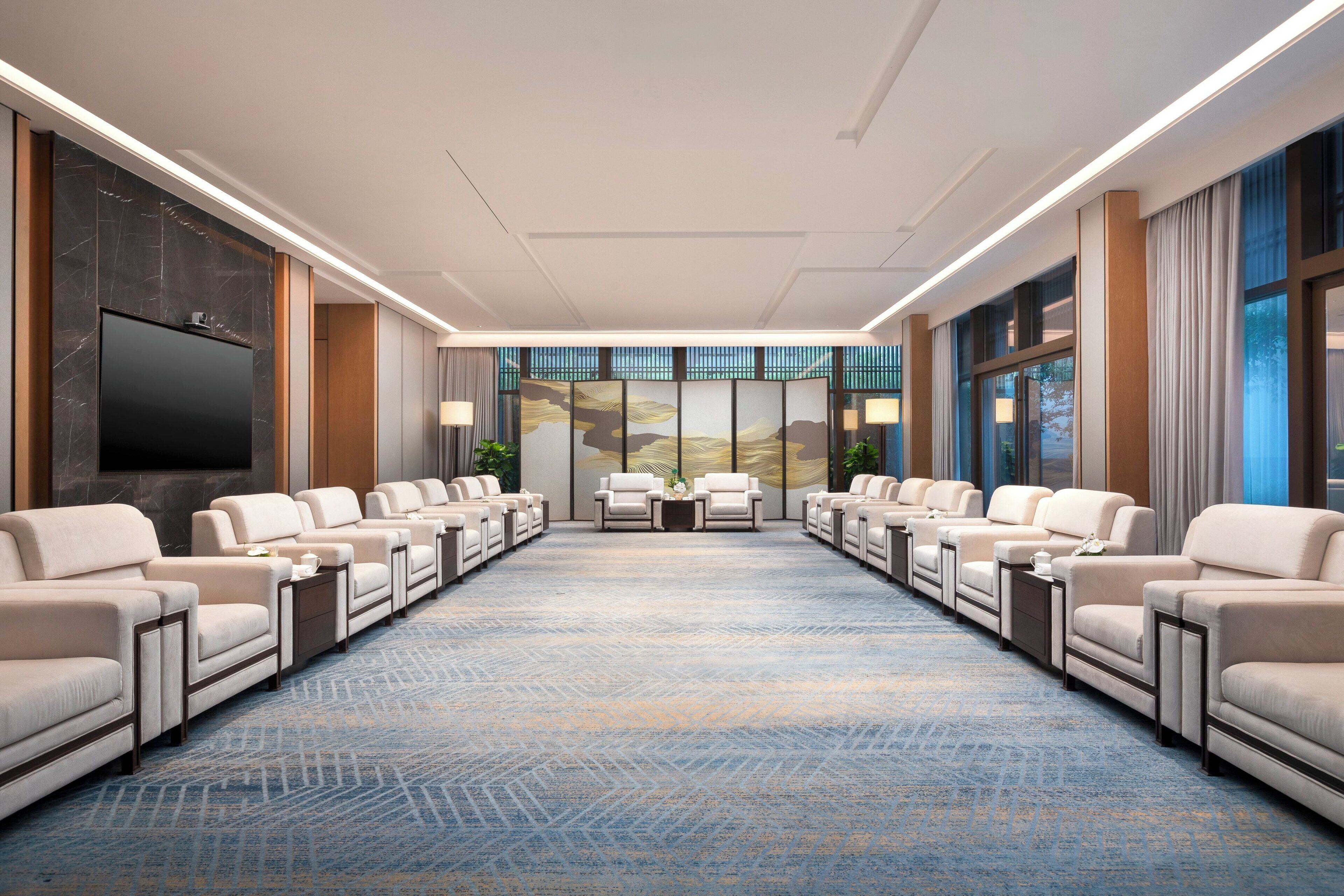 A hotel conference room with a long table, multiple sofas, and a large TV screen.