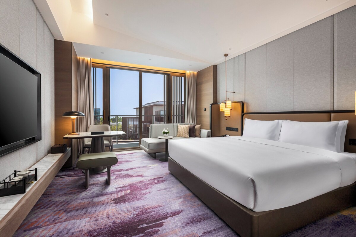 Ein Hotelzimmer mit einem großen Bett, einem Schreibtisch, einem Sessel, einer Couch und einem Fernseher.
