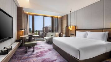 A hotel room with a large bed, a desk, a chair, a sofa, and a TV.