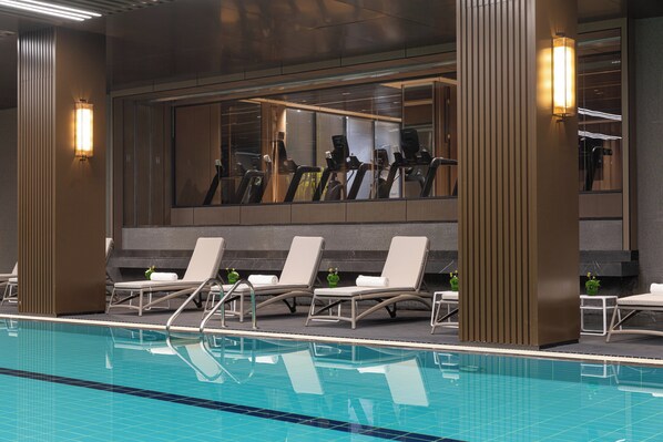 A swimming pool with lounge chairs and exercise equipment, surrounded by walls with large windows and wall-mounted lights. - Hualuxe Xianyang By Ihg (Xianyang)