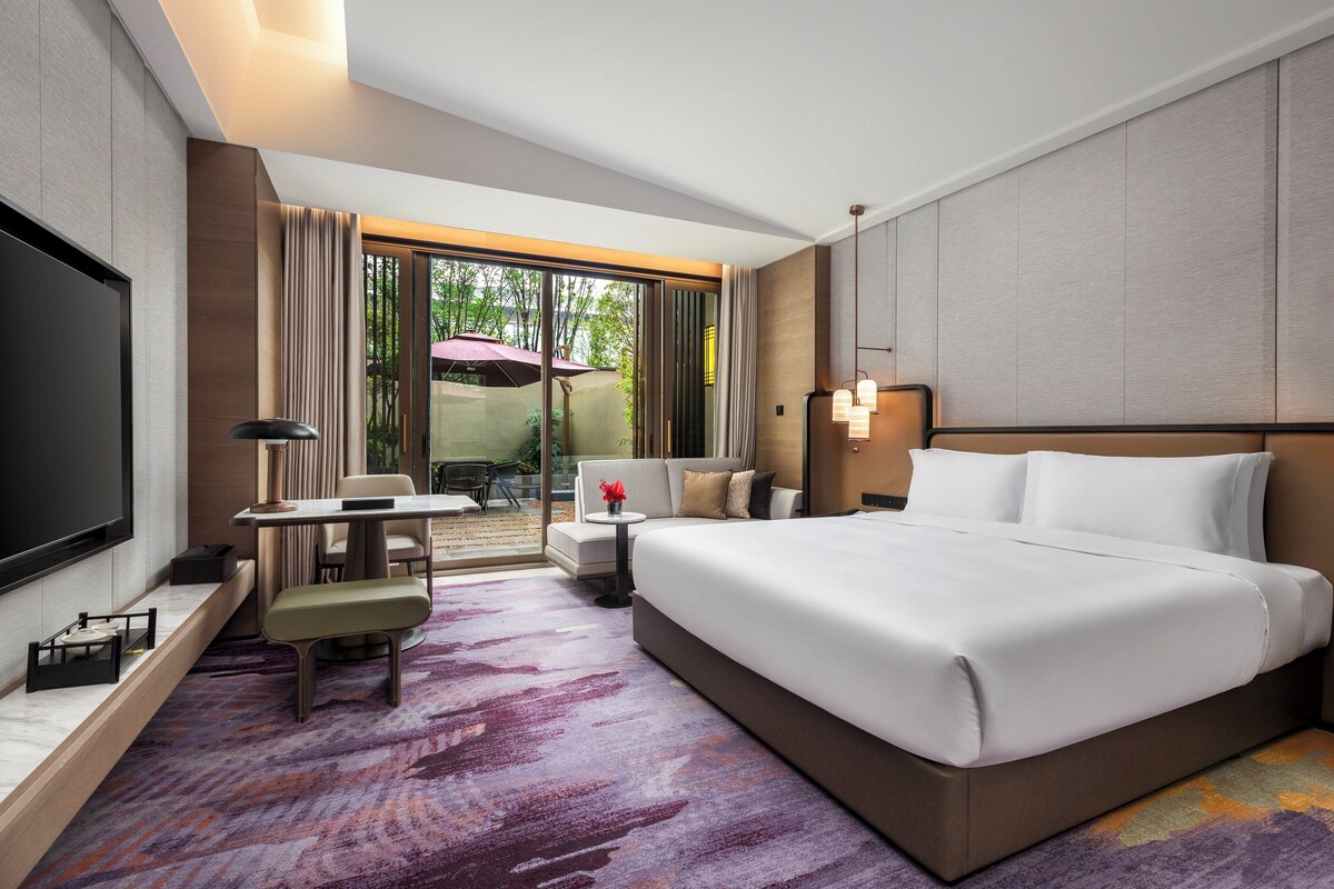 Habitación de hotel con una cama grande, un escritorio con silla, televisión y vista al exterior.