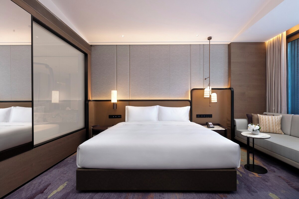 Ein modernes Hotelzimmer mit einem großen Bett, einer Sitzecke, einem kleinen Tisch und einem Nachttisch.