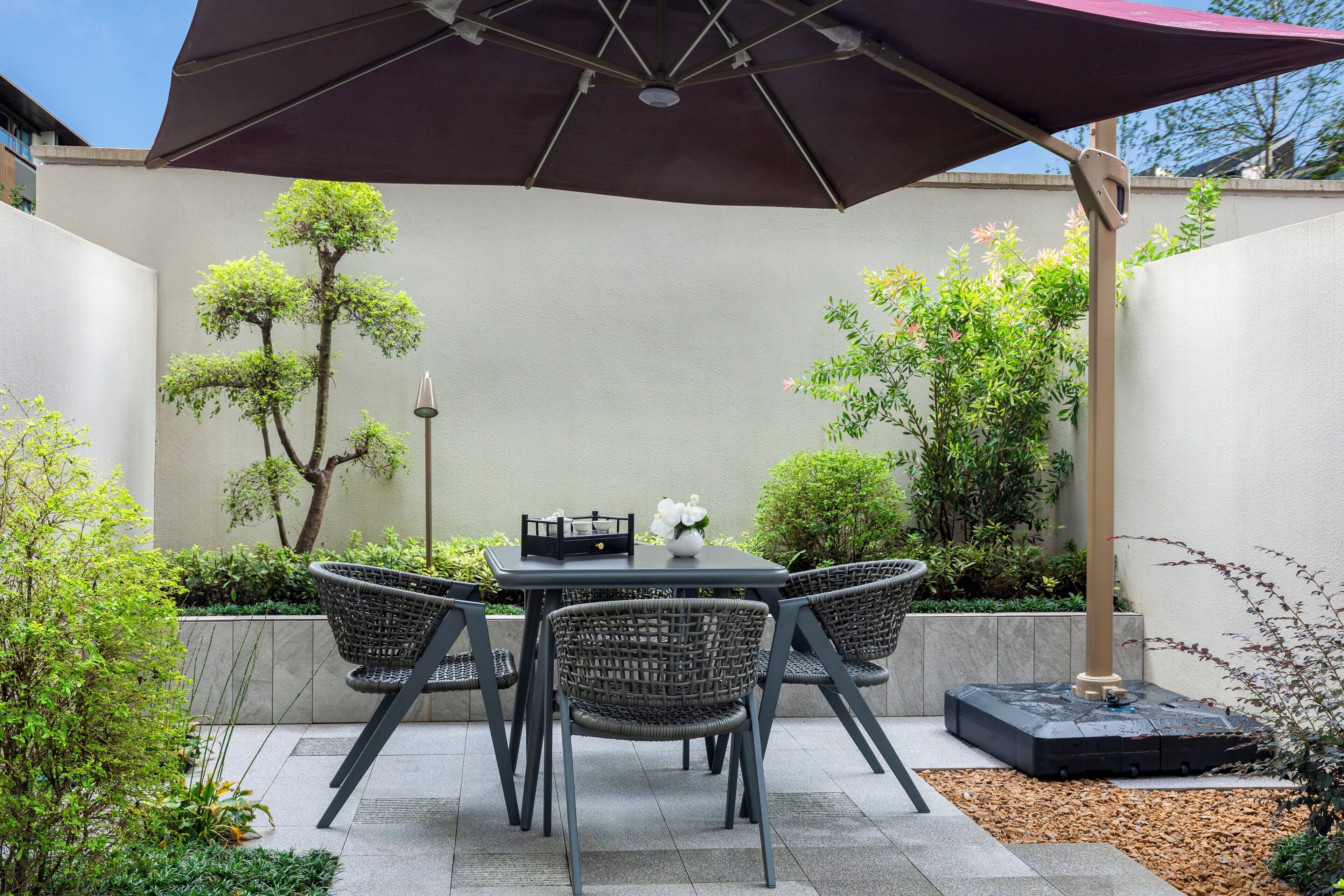 A patio with a table and chairs, surrounded by plants and a large umbrella.
