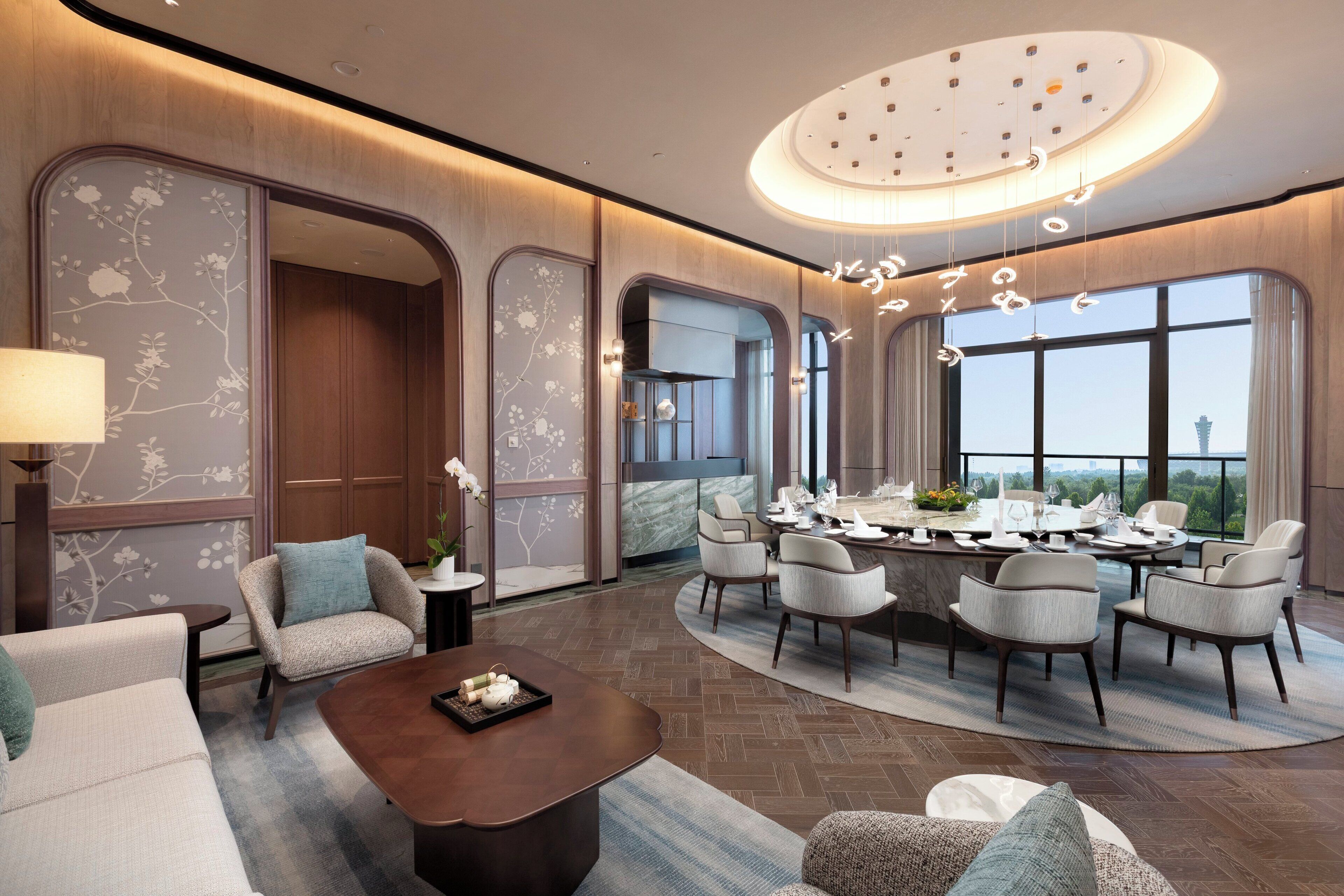 A modern hotel room with a dining area, a sofa, a coffee table, and a view of the cityscape.