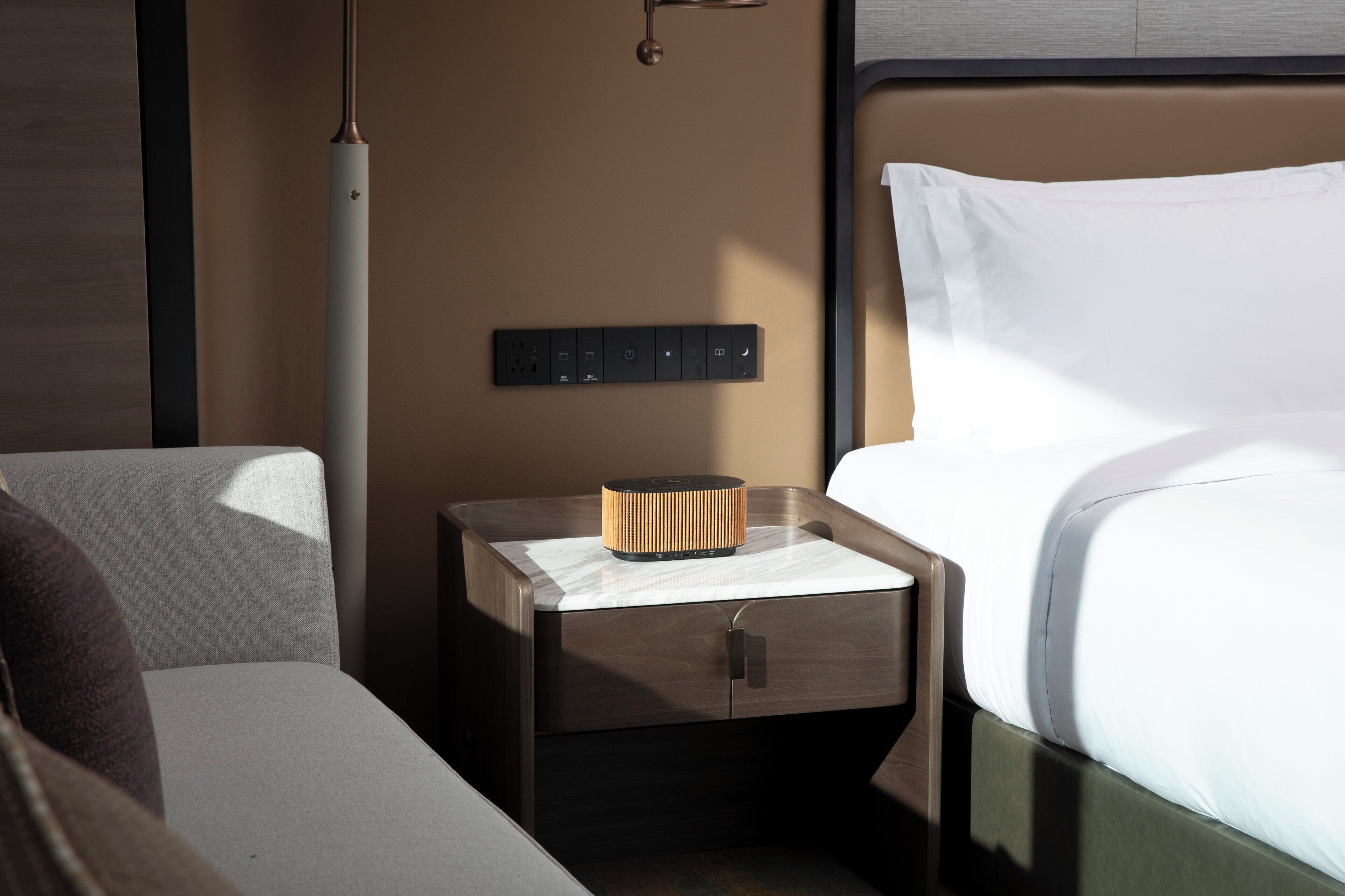 Une chambre d’hôtel bien rangée, avec un lit, une table de chevet dotée d’une lampe, une prise de courant et un petit meuble de rangement.