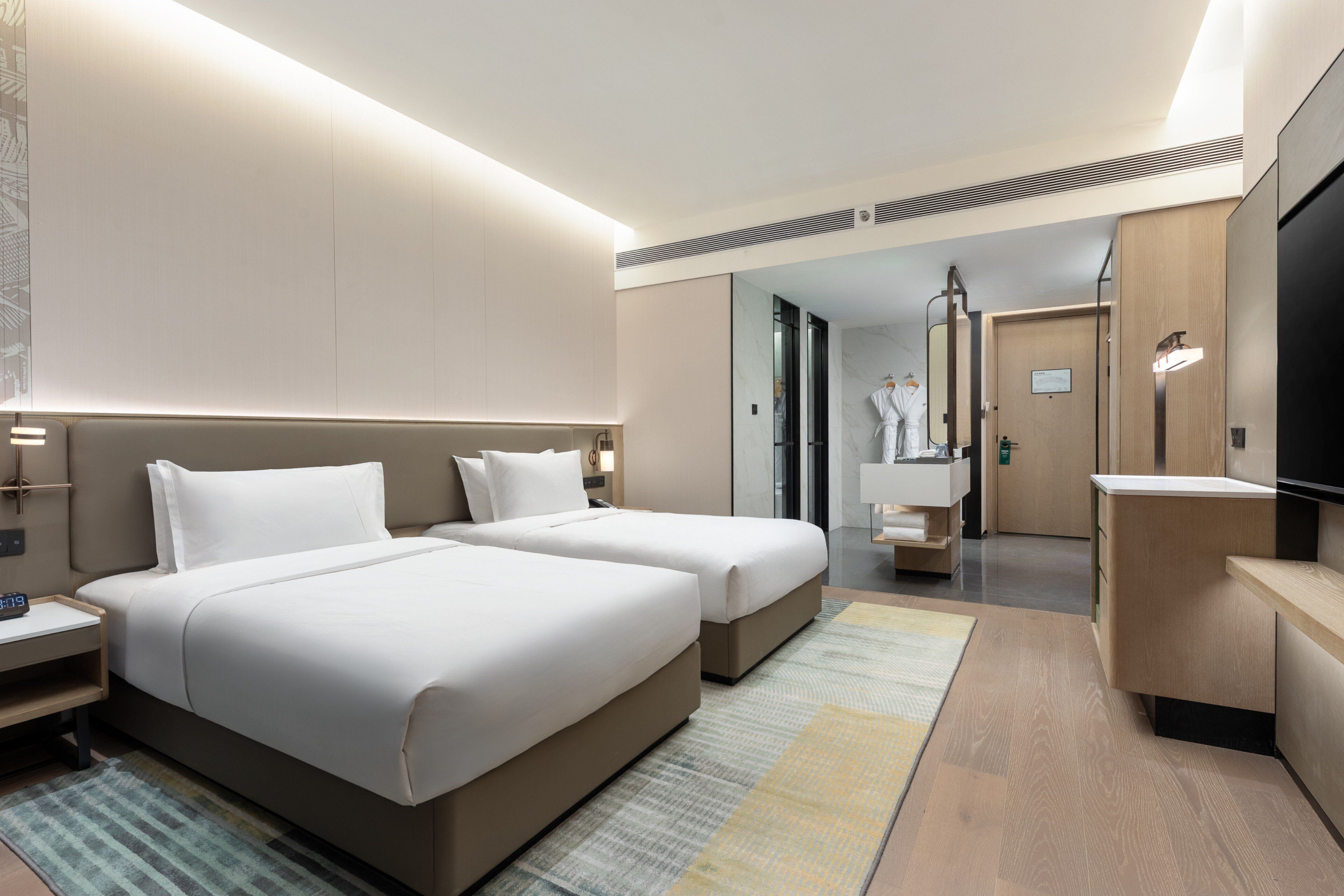 A hotel room with two beds, a TV, a desk, and a bathroom visible through an open door.
