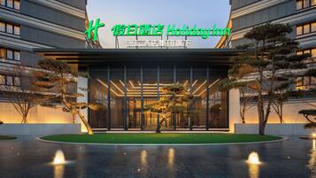 Une entrée d'hôtel moderne, avec une grande enseigne lumineuse, une pelouse bien entretenue et un élément décoratif aquatique à l'avant.