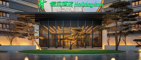 A modern hotel entrance with a large illuminated sign, a well-maintained lawn, and a water feature in front.